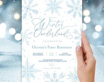 May include: A white rectangular birthday invitation card featuring light blue snowflake illustrations. The text reads: Join us in a Winter Onederland, Celebrating Oliver's First Birthday, Saturday 12 December, 10:00am-12:00pm, The Oak Manor Restaurant, 4483 Rockerfeller Street, Los Angeles, Ca 99321, RSVP Andrea at 251-555-2939.