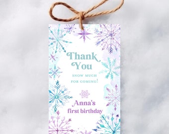 Op de afbeelding: Een rechthoekig cadeaulabel met een touwtje aan de bovenkant, voorzien van aquarel sneeuwvlokken in paarse en blauwgroene tinten op een witte achtergrond. De tekst luidt Thank You, SNOW MUCH FOR COMING!, en Anna's first birthday in het paars.
