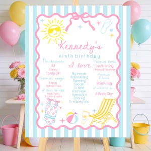 May include: A birthday milestone sign with a light blue and white striped background, featuring a pink scalloped border, a yellow sun, a beach chair, a beach ball, and text detailing Kennedy's ninth birthday, nicknames, and favorite things.