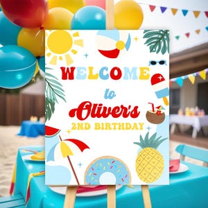 May include: A white welcome sign with a colorful beach theme. The sign says "Welcome to Oliver's 2nd Birthday" with a sun, beach ball, pineapple, donut, and palm tree illustrations.