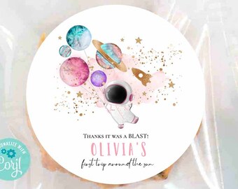 May include: A round sticker with a pink, blue, and gold watercolor design of planets, stars, and a rocket. The text "THANKS IT WAS A BLAST! OLIVIA'S first trip around the sun" is printed on the sticker.