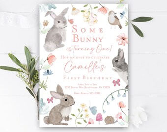 Puede incluir: Una invitación blanca con un diseño floral rosa y una ilustración de un conejo. El texto dice "Some Bunny is turning One! Hop on over to celebrate Camille's First Birthday. April 5th at 5pm. 9393 Bunny Way, Bunnyville, CA 93939. RSVP: Kim at 555-3932."