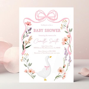 May include: A pink and white baby shower invitation featuring a floral wreath and a white goose with a pink bow. The invitation reads "kindly join us for a baby shower honouring the mom-to-be Camille Smith April 5th at 5pm 9393 Bunny Way, Bunnyville, CA 93939 RSVP Stacey at 555-3932 Registry at Your Store Here and Here"