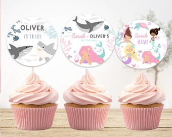 May include: Three cupcakes with pink frosting and pink paper liners. Each cupcake has a circular topper with a birthday theme. One topper says "Oliver is Four!" with shark and fish illustrations. The other two toppers feature mermaids and the text "Sarah is Five!" and "Sarah & Oliver's".
