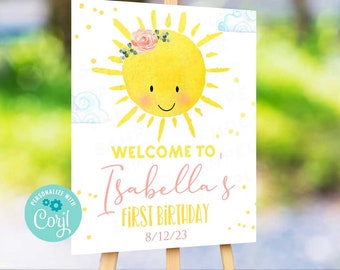 May include: A white welcome sign with a yellow sun with a pink flower crown. The sign says "Welcome to Isabella's First Birthday 8/12/23".