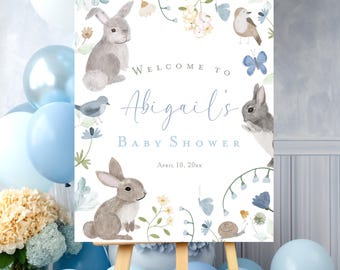 May include: A white welcome sign with blue and green floral accents and illustrations of bunnies, birds, and butterflies. The text reads "Welcome to Abigail's Baby Shower April 10, 20xx".