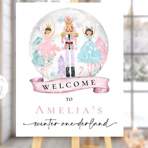 May include: A white welcome sign with pink and purple accents featuring a watercolor illustration of a nutcracker and two ballerinas inside a snow globe. The text reads "Welcome to Amelia's Winter Wonderland".