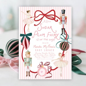 May include: A rectangular baby shower invitation card with a pink and white striped background. It features watercolor illustrations of two ballerinas, two nutcrackers, and three ornaments framed by a red ribbon. Text reads A Little Sugar Plum Fairy is on the way! Join us for Natalie McGrew's Baby Shower, Saturday, December 11th 10am, 1111 Nutcracker Street, Butterville, Registry: Babystone & Target, RSVP: Natalie at 212-555-9999.