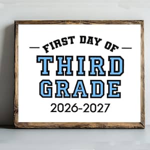 May include: A rectangular sign in a dark wood frame featuring the text FIRST DAY OF THIRD GRADE in black and light blue block lettering, with the school year 2026-2027 printed in black at the bottom against a white background.