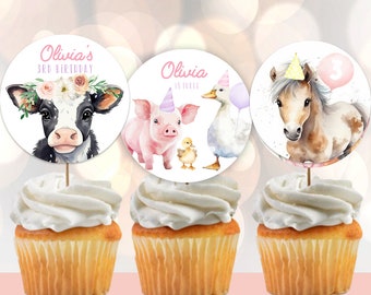 Könnte beinhalten: Drei Cupcake-Topper mit Bauernhoftieren. Die Topper sind rund und haben einen weißen Hintergrund mit Aquarell-Illustrationen einer Kuh, eines Schweins und eines Pferdes. Die Kuh trägt eine Blumenkrone und das Pferd einen Partyhut. Der Text auf den Toppern lautet "Olivia's 3rd Birthday" und "Olivia is three".