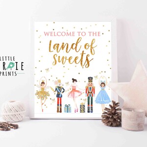 Puede incluir: Una impresión enmarcada con el texto "Welcome to the Land of Sweets" en letras doradas con purpurina. La impresión presenta ilustraciones de acuarela de bailarinas de ballet, un cascanueces y un rey ratón. El logotipo de Little Birdie Prints está en la esquina.