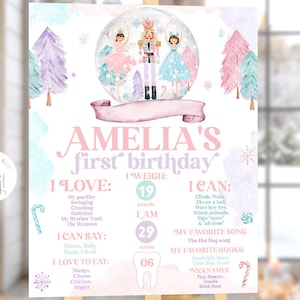 May include: A pink and purple first birthday sign with a watercolor background. The sign features a snow globe with a Nutcracker and two ballerinas. The sign also includes the name Amelia, the child's age, weight, and favorite things.