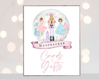 May include: A pink and blue watercolor illustration of a Nutcracker and two ballerinas inside a snow globe. The text "Nutcracker" is written on a pink ribbon below the snow globe. The text "Cards & Gifts" is written in pink cursive below the ribbon.