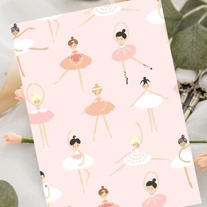 May include: Pink wrapping paper with a repeating pattern of ballerinas in various poses wearing pink, white and gold tutus. The ballerinas have brown, black and blonde hair.