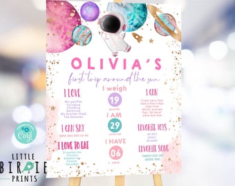 May include: A pink and blue space-themed first birthday poster with gold glitter accents. The poster features a watercolor illustration of planets and stars. The text on the poster reads "Olivia's first trip around the sun". The poster also includes information about Olivia's age, weight, height, favorite toys, and favorite song.
