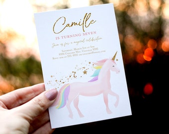 May include: A white invitation card with gold glitter text that reads "Camille is turning seven. Join us for a magical celebration. Saturday, March 5th at 5pm. 9394 Unicorn Way, Univille 9392. RSVP Kim at 555-9931 or unicorn@email.com". The card features a pink unicorn with a rainbow mane and tail, and gold glitter stars.