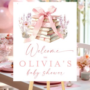 Pode incluir: Uma placa de boas-vindas para chá de bebê com uma ilustração em aquarela de uma pilha de livros amarrados com uma fita rosa e detalhes florais. A placa diz "Bem-vindo ao chá de bebê de Olivia" em um elegante script rosa.