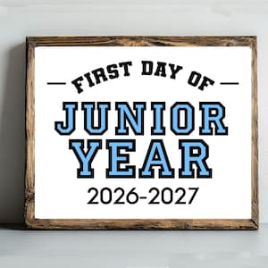 May include: A rectangular sign with a dark wood frame featuring the black text FIRST DAY OF and the light blue text JUNIOR YEAR in a bold collegiate font, followed by the black text 2026-2027 centered on a white background.
