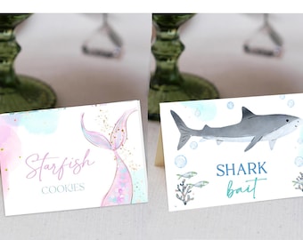 May include: Two watercolor-style table cards with ocean themes. The first card features a pink and purple mermaid tail with gold glitter and the text "Starfish Cookies". The second card features a gray shark with blue bubbles and the text "Shark Bait".