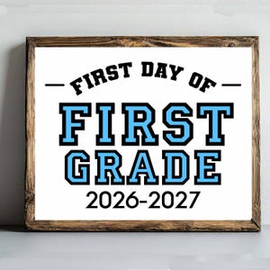 Könnte beinhalten: Ein gerahmtes Schild mit weißem Hintergrund und einem Rahmen aus dunklem Holz. Der Text lautet FIRST DAY OF in Schwarz, gefolgt von FIRST GRADE in großen hellblauen Blockbuchstaben mit schwarzer Umrandung und dem Schuljahr 2026-2027 unten.