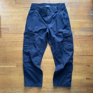 May include: Navy blue cargo pants with multiple pockets on the legs and sides. The pants have a belt and a button closure. The fabric appears to be a durable, woven material.