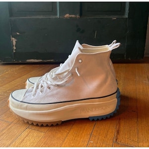 Peut inclure: Baskets montantes blanc cassé avec des semelles épaisses et texturées. Les semelles combinent beige, marron et bleu. Le mot "JW ANDERSON" est imprimé sur le côté. Les baskets ont des lacets blancs et une tige en toile.