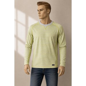 Op de afbeelding: Een lichtgroen shirt met lange mouwen en gele horizontale strepen. Het shirt heeft een grijze halslijn en manchetten, en een kleine rechthoekige patch. Het model draagt een blauwe jeans.