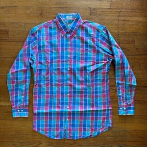 May include: A long-sleeve button-down shirt featuring a vibrant plaid pattern in shades of bright blue, magenta, and yellow. The shirt has a classic collar, a full-length front button placket, and buttoned cuffs on each sleeve, all in a consistent grid.