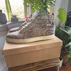 Könnte beinhalten: High-Top-Sneakers mit Schlangenmuster in Braun- und Beigetönen. Die Schuhe haben eine weiße Sohle und sind geschnürt. Sie stehen auf einem Karton.