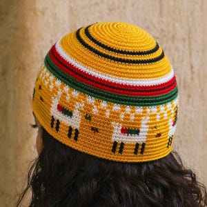 May include: A yellow crocheted skullcap with a colorful striped band and a pattern of white llamas. The hat has a black, red, green, and white striped band. The llama pattern is on the lower portion of the hat.