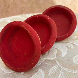 Puede incluir: Tres cuencos pequeños y redondos de madera roja están dispuestos sobre una superficie estampada. Los cuencos tienen un diseño sencillo y clásico con un aspecto ligeramente desgastado, lo que sugiere que son hechos a mano o vintage. El color rojo vibrante contrasta con el fondo neutro.