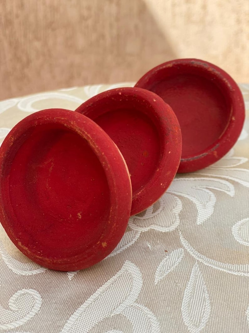 Puede incluir: Tres cuencos peque&ntilde;os y redondos de madera roja est&aacute;n dispuestos sobre una superficie estampada. Los cuencos tienen un dise&ntilde;o sencillo y cl&aacute;sico con un aspecto ligeramente desgastado, lo que sugiere que son hechos a mano o vintage. El color rojo vibrante contrasta con el fondo neutro.