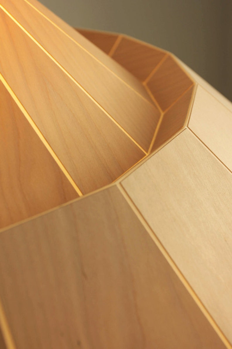 May include: A close-up of a wooden lampshade with a geometric design. The lampshade is made of light-colored wood and has a smooth, polished finish.
