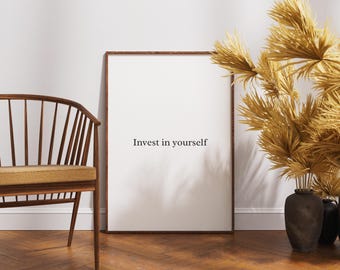 Könnte beinhalten: Ein gerahmter Druck mit dem Text "Invest in yourself" in einer Raumeinstellung. Der Druck lehnt an einer weißen Wand, neben einem Holzstuhl und einer Vase mit getrockneten Pflanzen. Der Raum hat eine warme, einladende Atmosphäre.