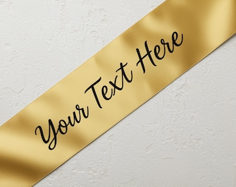 May include: A gold satin sash with the text "Your Text Here" in a black script font. The sash is angled across a white textured background, creating a simple yet elegant design.