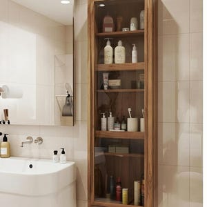 以下が含まれることがあります： ガラス扉付きの木製バスルームキャビネット。タイル張りの壁に取り付けられています。キャビネットには、ボトル、瓶、チューブなど、さまざまな化粧品が収納されています。キャビネットは温かみのある茶色で、いくつかの棚があります。