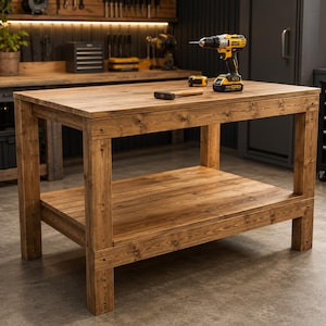 May include: A sturdy, wooden workbench with a lower shelf. The workbench is made of light brown wood and has a rectangular top. A cordless drill, hammer, and tape measure rest on the surface. The workbench is in a workshop setting.
