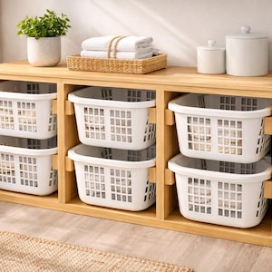 May include: A wooden storage unit with six white laundry baskets. The unit has a light wood finish and a top shelf with a small potted plant, a woven basket with folded towels, and two white ceramic containers.