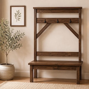 Könnte beinhalten: Ein dunkelbrauner Garderobenständer aus Holz mit einer Bank, Haken und einem oberen Regal. Der Garderobenständer hat ein rustikales Design und steht vor einer hellen Wand. Ein gerahmter botanischer Druck und eine Topfpflanze sind ebenfalls zu sehen.