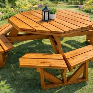 Può includere: Un tavolo da picnic in legno con panche attaccate. Il tavolo ha un piano ottagonale ed è realizzato in legno marrone chiaro. Una piccola lanterna nera e una pianta in vaso sono sul tavolo. Il tavolo è su un prato verde.