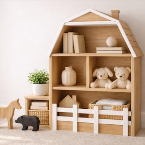 Puede incluir: Una estantería de madera con forma de casa con varios estantes, que contiene libros, objetos decorativos y peluches. Un pequeño caballo, un oso y un ternero de madera están frente a la estantería. La estantería tiene una valla blanca.