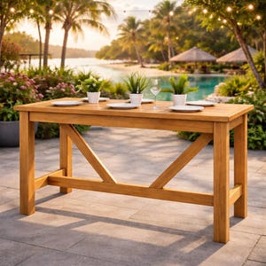 May include: A rectangular wooden outdoor dining table with a natural finish. The table has a cross-brace design on the legs. White plates, small potted plants, and a wine glass are set on the table. The background features a tropical setting with palm trees and a pool.
