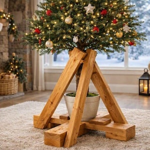 May include: A wooden Christmas tree stand constructed from thick, light brown timber beams arranged in a sturdy, cross-shaped base with angled supports that cradle a round, light-colored pot holding a decorated evergreen tree with lights.