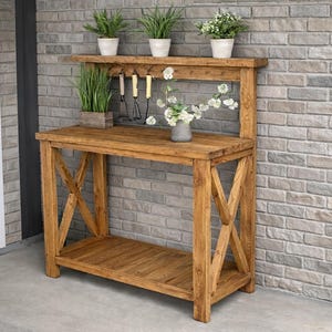 May include: A rustic wooden potting bench with a lower shelf and an upper shelf holding potted plants. The bench has an X-shaped support on the sides and includes hanging garden tools. The wood has a warm, natural finish.