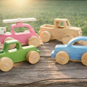 May include: Four colorful wooden toy vehicles: a pink helicopter, a tan pickup truck, a green truck, and a blue car. Each toy has wooden wheels and is painted in bright colors. The toys are arranged on a wooden surface.