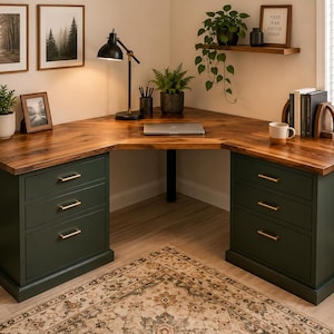 May include: A dark green corner desk with a wooden top, featuring three drawers on each side with gold-colored handles. The desk is in a well-lit room with plants, artwork, and a rug.