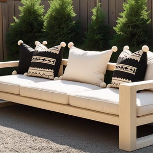 Puede incluir: Un sofá de exterior de madera clara con cojines color crema y cojines decorativos. Los cojines incluyen cojines de color crema liso y cojines negros con un diseño geométrico. A la izquierda hay una pequeña mesa auxiliar negra.