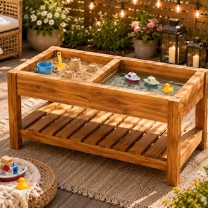 May include: A rectangular wooden sensory table with two separate compartments, one filled with sand and a yellow shovel, and the other filled with water containing two toy boats and a yellow rubber duck. The table features a slatted lower shelf.
