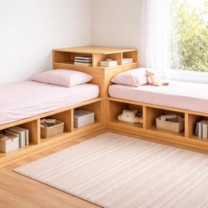 Op de afbeelding: Twee houten platformbedden met ingebouwde opbergruimte. Elk bed heeft een roze hoeslaken en kussen. De bedden zijn in een L-vorm gerangschikt, met een gedeeld hoofdbord. De opbergvakken bevatten manden, dozen en decoratieve items.