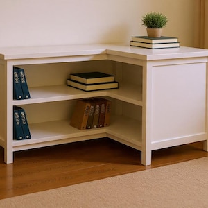 May include: A white corner desk with open shelving and a solid door. The desk has a flat top with a small potted plant and books. The shelves hold books and binders. The desk is made of wood and sits on a hardwood floor.